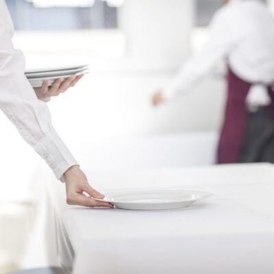 Pracownik układa talerze na stole, świadcząc usługi cateringowe.