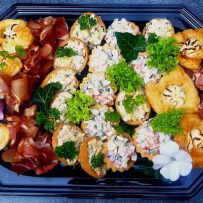 Na talerzu znajduje się elegancki catering na przyjęcia z różnymi przekąskami, takimi jak wędliny i wytrawne ciasta.