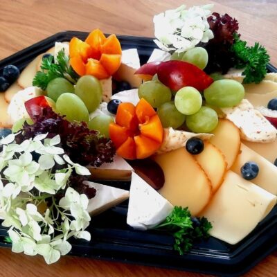 Deski serów z owocami i ziołami na czarnej tacy.