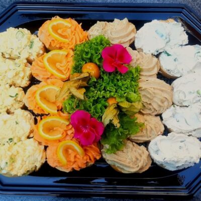 Tacki cateringowe z różnorodnymi przystawkami udekorowane kwiatami i owocami.