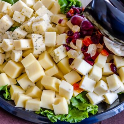 Deski serów z różnorodnymi kostkami i owocami na liściach sałaty.