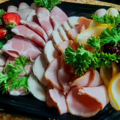 Tacki cateringowe z różnorodnymi wędlinami i dekoracjami z ziół.